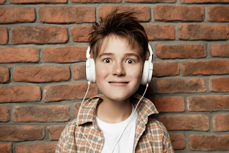 A portrait of a young boy with headphones in casual clothes posing over the brick wall. Fashion for male teenagers.の写真素材