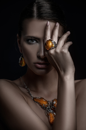 A close up portrait of a beautiful young dark-haired woman posing in the studio over the black background. Beauty, cosmetics, skincare, jewelry.の写真素材