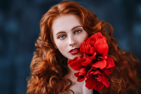 A close up portrait of a lovely beautiful girl with a big red flower. Beauty, cosmetics.の写真素材