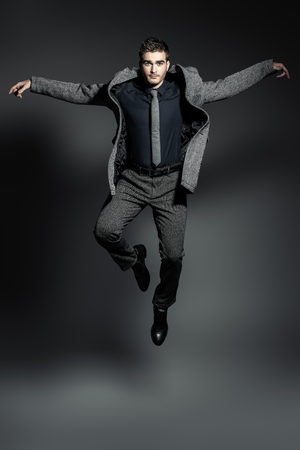 A full length portrait of a fashionable young man jumping in the studio over the grey background. Formal fashion for men.の写真素材