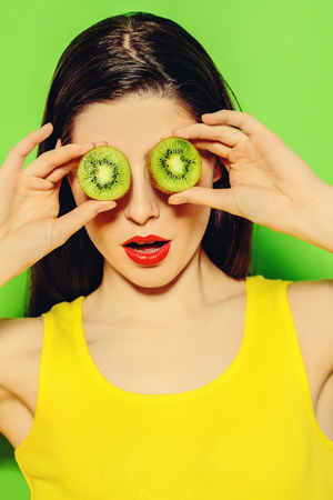 A portrait of a bright beautiful girl with kiwi posing in the studio over the green background. Beauty, health.の写真素材