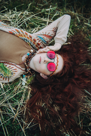 A portrait of a fashion female model lying on the grass. Contemporary bohemian style. Spirit of freedom. Fashion shot. Bohemian, bo-ho style.の写真素材