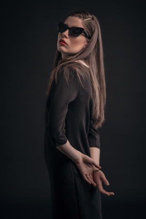 A portrait of a beautiful dark-haired young woman in sunglasses posing over the black background. Beauty, cosmetics, fashion.の写真素材