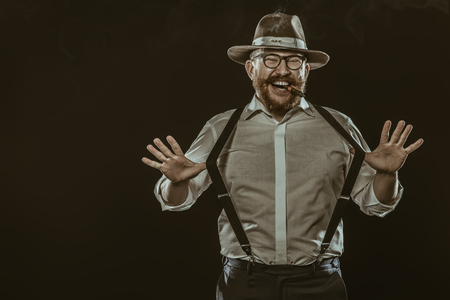 A portrait of a laughing man with a cigar posing in the studio over the black background. Men's beauty, fashion.の写真素材