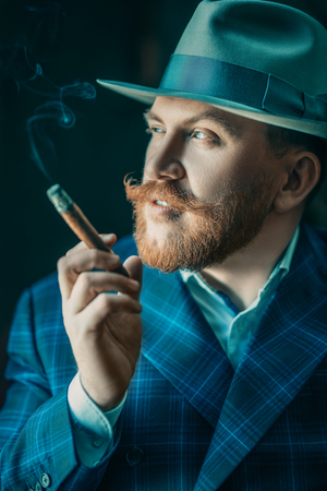 A close up portrait of a thoughtful man with a cigar posing in the studio over the black background. Men's beauty, fashion, style.の写真素材