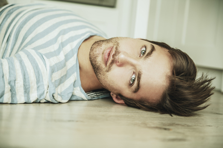 A close up portrait of a handsome dreamy man lying on the floor. Home, casual fashion.の写真素材