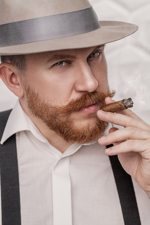 A close up portrait of a thoughtful man with a cigar posing in the studio over the white background. Men's beauty, fashion, style.の写真素材