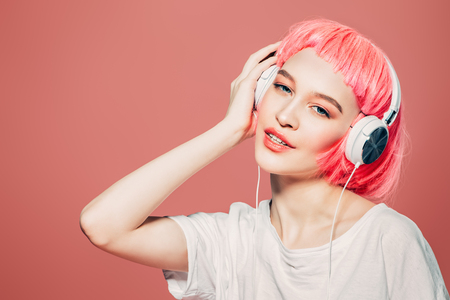Trendy girl with pink hair enjoys the music on headphones. Pink background. Youth style, leisure.の写真素材
