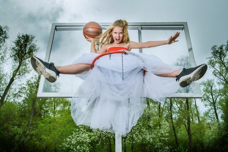 A full length portrait of a sporty teenager girl posing on the basketball pinch in a white fluffy skirt. Sport fashion, active lifestyle, basketball.の写真素材