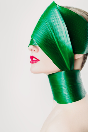 A close up portrait of a beautiful girl with a head rolled up in a leave posing in the studio over the white background. Beauty, nature, make up.の写真素材