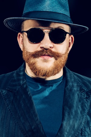 A close up portrait of a stylish man in sunglasses posing in the studio over the black background. Men's beauty, fashion, style, optics.の写真素材