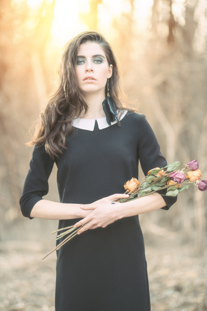 A portrait of a beautiful mysterious girl in black posing  with flowers in the forest. Beauty, fashion, nature.の写真素材