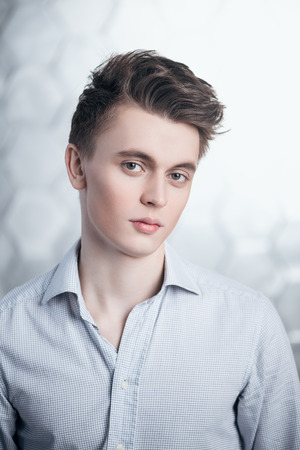 A close up portrait of a young guy in a shirt posing indoor. Fashion and beauty for men.の写真素材