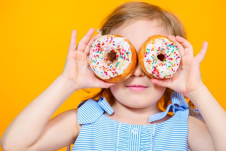A close up portrait of a pretty girl having fun with donuts in the studio over the yellow background. Kids, beauty, food, sweets.の写真素材