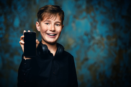 A portrait of a young boy with a smartphone and headphones. Fashion, gadgets.の写真素材