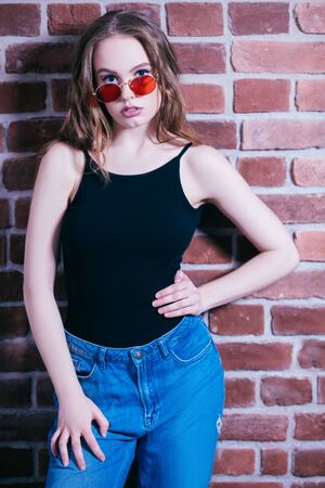 A portrait of a young beautiful woman in sunglasses posing in the studio over the brick wall. Casual fashion, beauty, optics.の写真素材