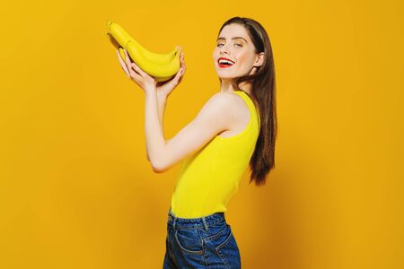 A portrait of a bright beautiful girl with a banana posing in the studio over the yellow background. Beauty, health.の写真素材