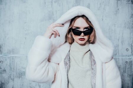 A portrait of a beautiful woman wearing a white fur coat with hood and sunglasses. Beauty, winter fashion, style.の写真素材