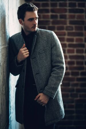 A portrait of a thoughtful fashionable young man near the wall. Casual fashion for men.の写真素材