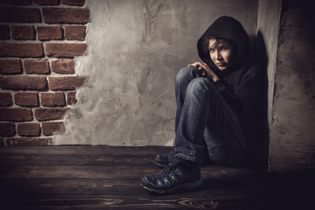 A full length portrait of a young boy in a hood posing near the wall in the corner. Kids, fashion,...