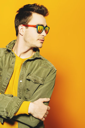 A portrait of a fashionable young man posing in the studio over the yellow background. Casual...