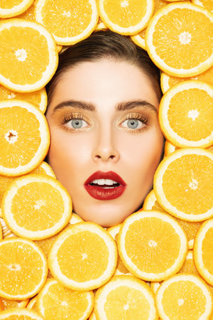 A portrait of a bright beautiful girl with juicy oranges posing in the studio over the yellow...