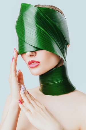 A close up portrait of a beautiful girl with a head rolled up in a leave posing in the studio over the white background. Beauty, nature, make up.の写真素材