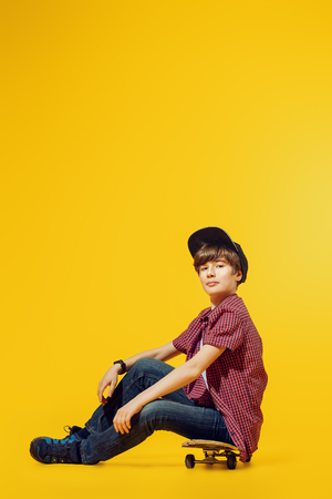 A full length portrait of a bright young boy posing in the studio over the yellow background with a skateboard. Kids, fashion.の写真素材