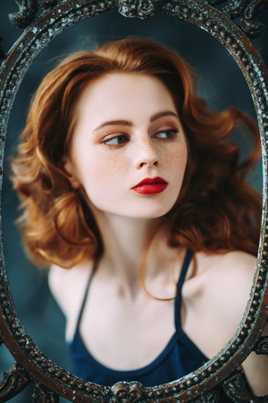 A portrait of a gorgeous beautiful young woman looking through the frame of the mirror. Beauty, cosmetics.の写真素材