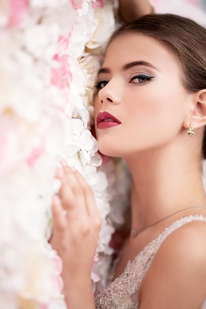 A close up portrait of a dreamy lady in a wedding dress posing indoor over the flowers. Wedding, beauty, fashion.の写真素材