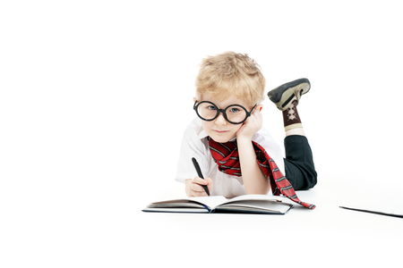 A portrait of a focused young schoolboy writing in the notebook. Kids fashion for school, stationery, education.の写真素材