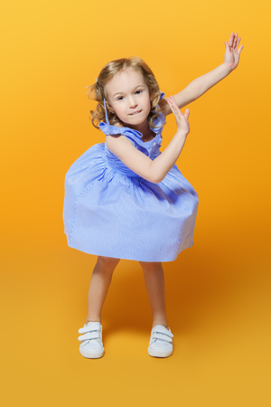 A full length portrait of a pretty girl in a blue dress posing in the studio over the yellow background. Kids, fashion, beauty.の写真素材