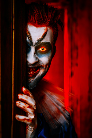 A close up portrait of an angry clown from a horror film hiding behind a door. Halloween, carnival.の写真素材