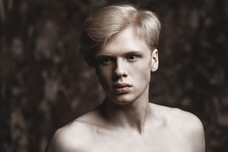 Portrait of a shirtless young man with blond hair posing at studio over grunge background. Men's beauty and health.の写真素材