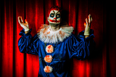 A portrait of an angry crazy clown from a horror film over the red curtain. Halloween, carnival.の写真素材