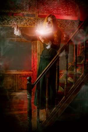 A portrait of an angry witch with a spellbook on the stairs in her den. Magic, dark force, spell.の写真素材