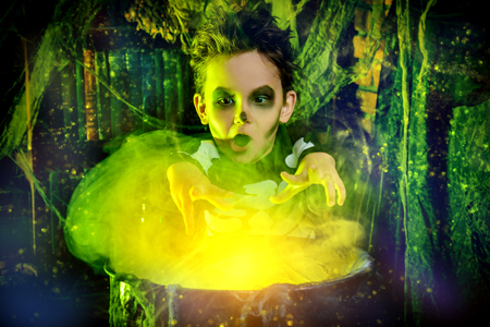 Happy Halloween. Funny child boy in a costume of skeleton cooks a magic potion in a witch's lair.の写真素材