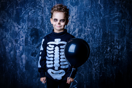 Portrait of a funny little boy in a costume of skeleton holding black balloon. Happy Halloween!の写真素材