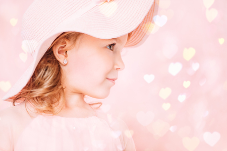 A close up portrait of a pretty happy girl in a pink dress posing in the studio over the pink background. Kids, fashion, beauty.の写真素材