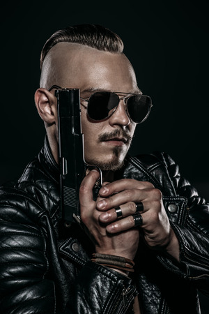 Dark portrait of a serious gangster man with  gun wearing black leather jacket.の写真素材