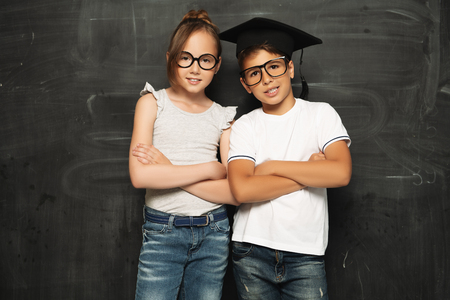 A portrait of two cheerful young pupils over the blackboard in a classroom. Beauty, fashion, school, education.の写真素材