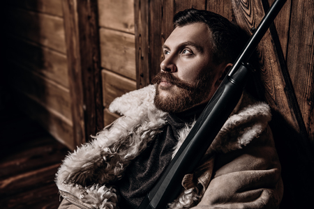A portrait of a hunter man standing at the wooden house. Man, hunting, musket.の写真素材