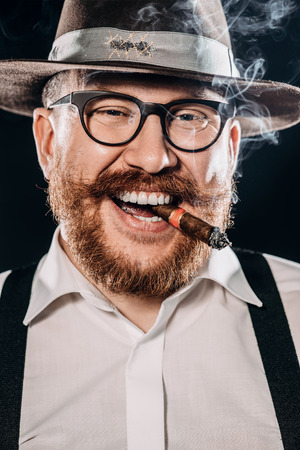 A close up portrait of a happy man with a cigar posing in the studio over the black background. Men's beauty, fashion, style.の写真素材