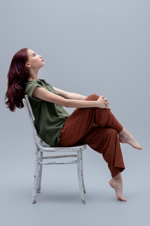 A full length portrait of a beautiful young woman on the chair over the grey background in the studio. Casual fashion.の写真素材