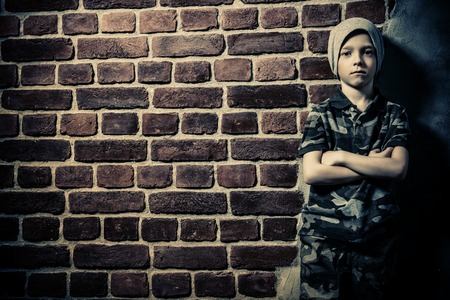 A portrait of a handsome child boy posing in the studio over the brick wall background. Kids, fashion, military style, beauty.の写真素材