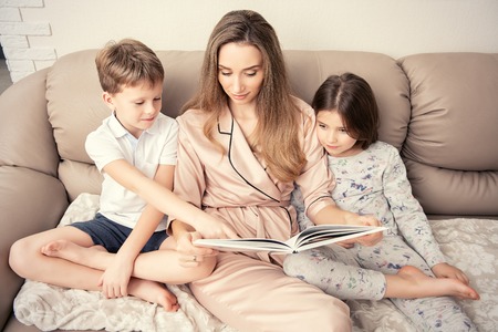 Mom is with her children sitting on the sofa in the room. Family home shoot.の写真素材