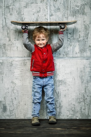 A full length portrait of a happy young schoolboy posing in the studio over the grey background with a skateboard. Kids casual fashion, education.の写真素材