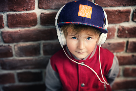 A portrait of a young schoolboy posing in the studio over the brick wall and listening to music in the headphones. Kids casual fashion, education.の写真素材