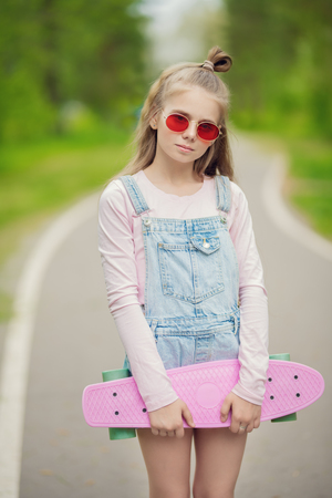 A portrait of an active teenager girl posing on the road with a skateboard. Casual kids fashion, active lifestyle.の写真素材