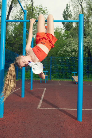 A portrait of a sporty teenager girl posing on the horizontal bar with a mouthpiece. Sport fashion,...